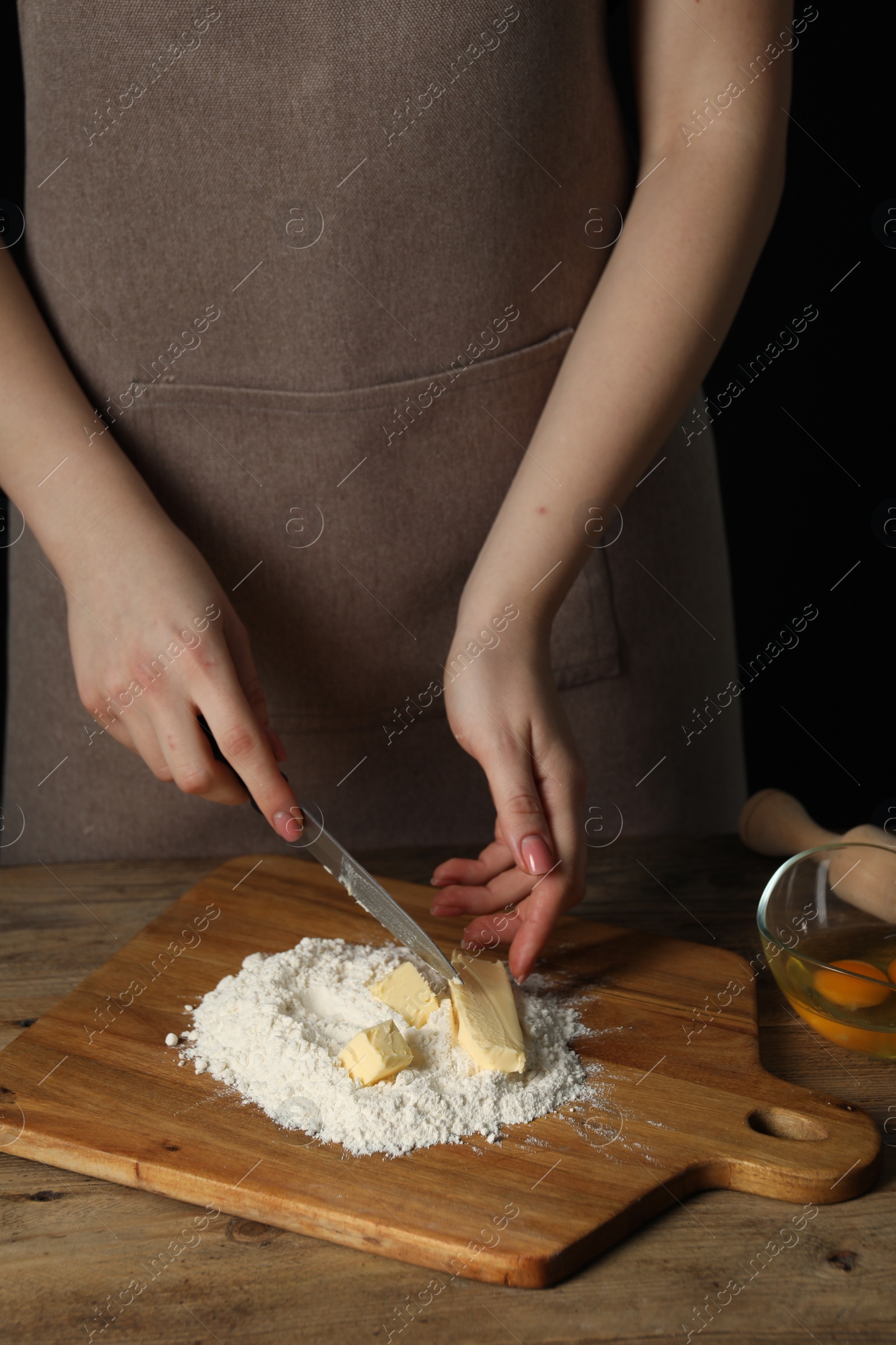 Photo of Woman cutting fresh butter at wooden table, closeup