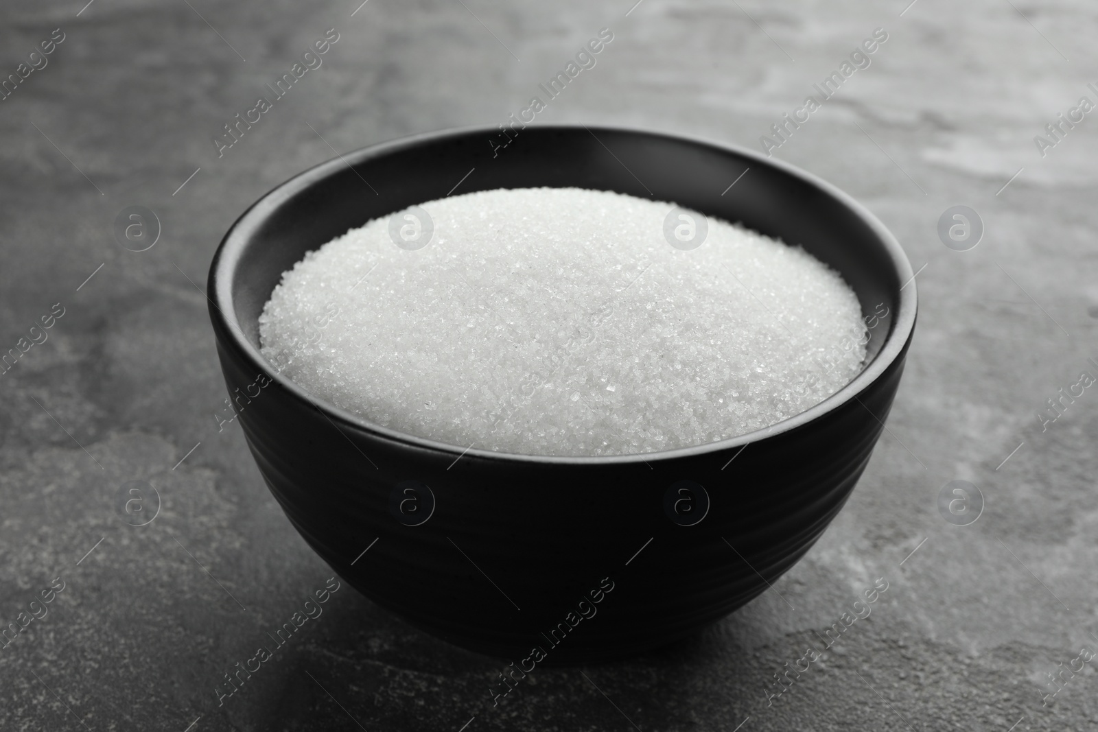 Photo of Granulated sugar in bowl on grey textured table, closeup