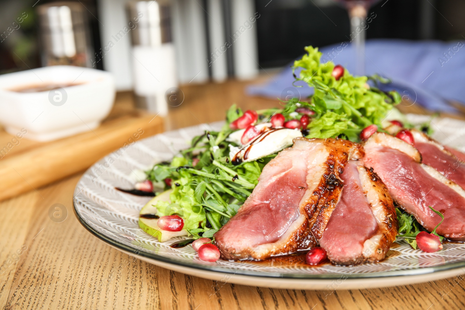 Photo of Delicious salad with roasted duck breast served on wooden table indoors, closeup