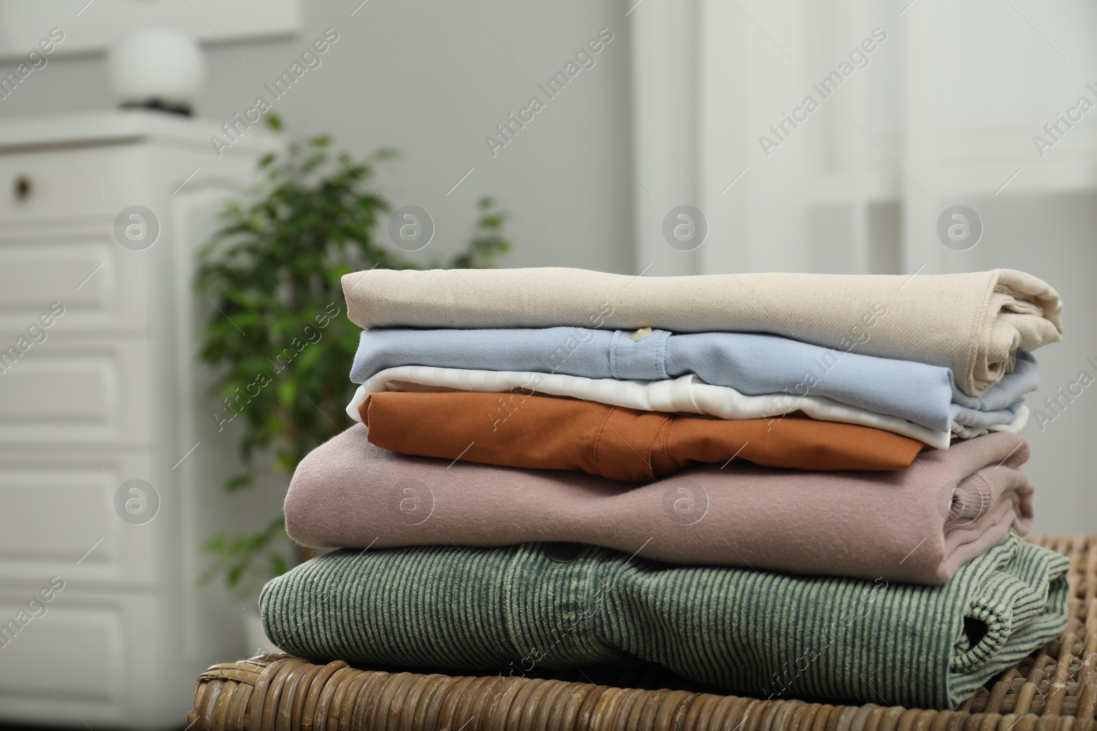 Photo of Sorting and organizing. Stack of different folded clothes on wicker table indoors, closeup