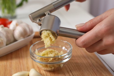 Photo of Woman squeezing garlic with press at wooden table, closeup