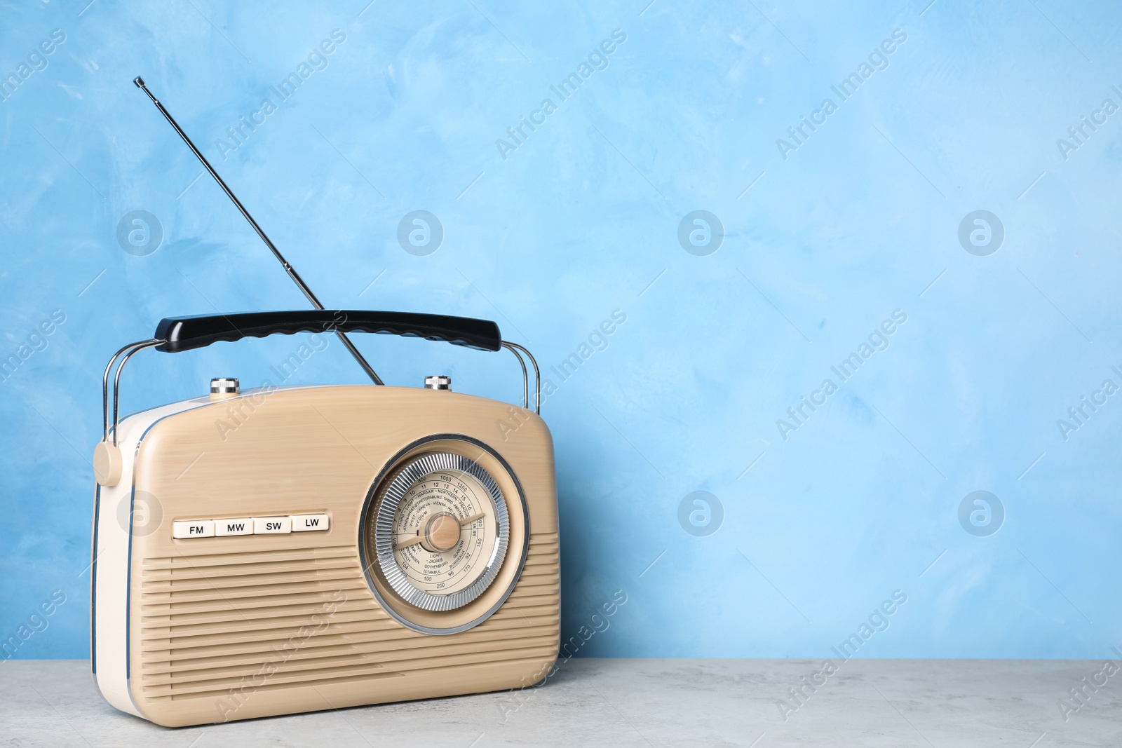 Photo of Retro radio receiver on grey table against light blue background. Space for text