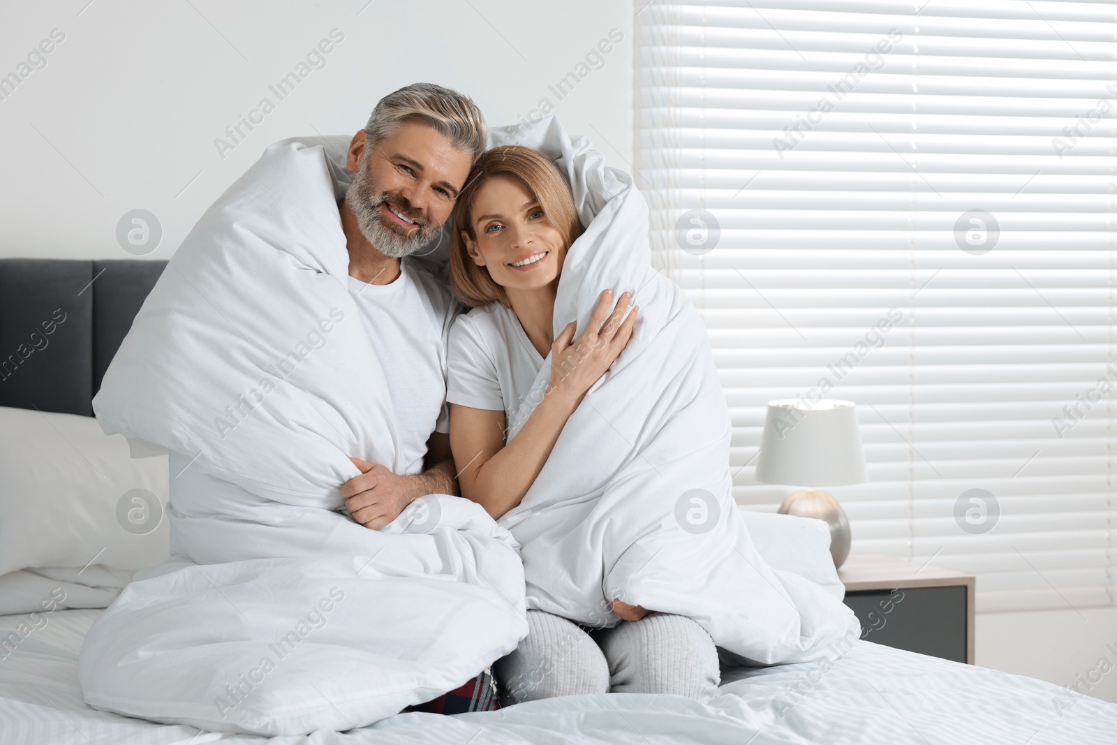 Photo of Lovely mature couple wrapped in blanket on bed at home