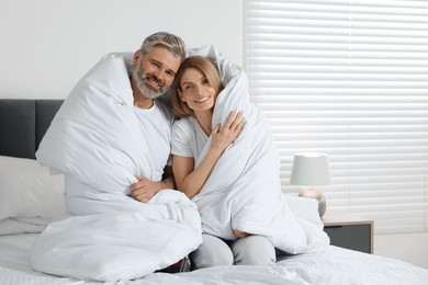 Lovely mature couple wrapped in blanket on bed at home