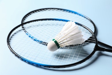 Photo of Feather badminton shuttlecock and rackets on light blue background, closeup