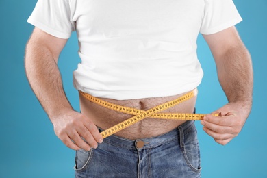 Photo of Overweight man with large belly and measuring tape on color background, closeup