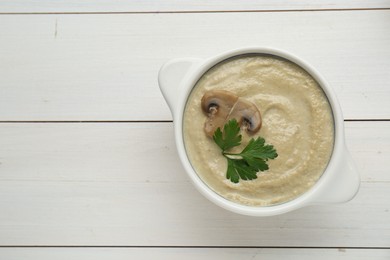 Delicious mushroom cream soup with parsley on white wooden table, top view. Space for text