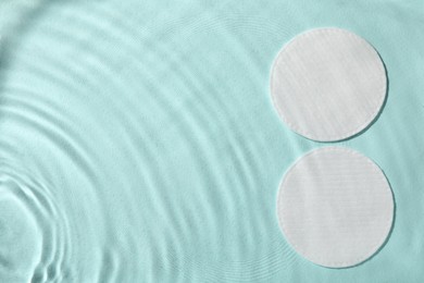 Photo of White cotton pads in water on turquoise background, flat lay. Space for text