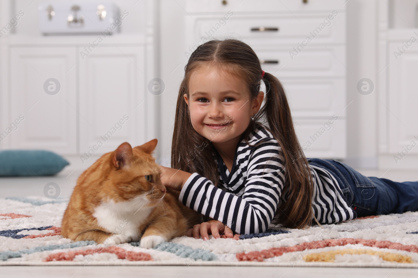 Photo of Happy little girl petting cute ginger cat on carpet at home