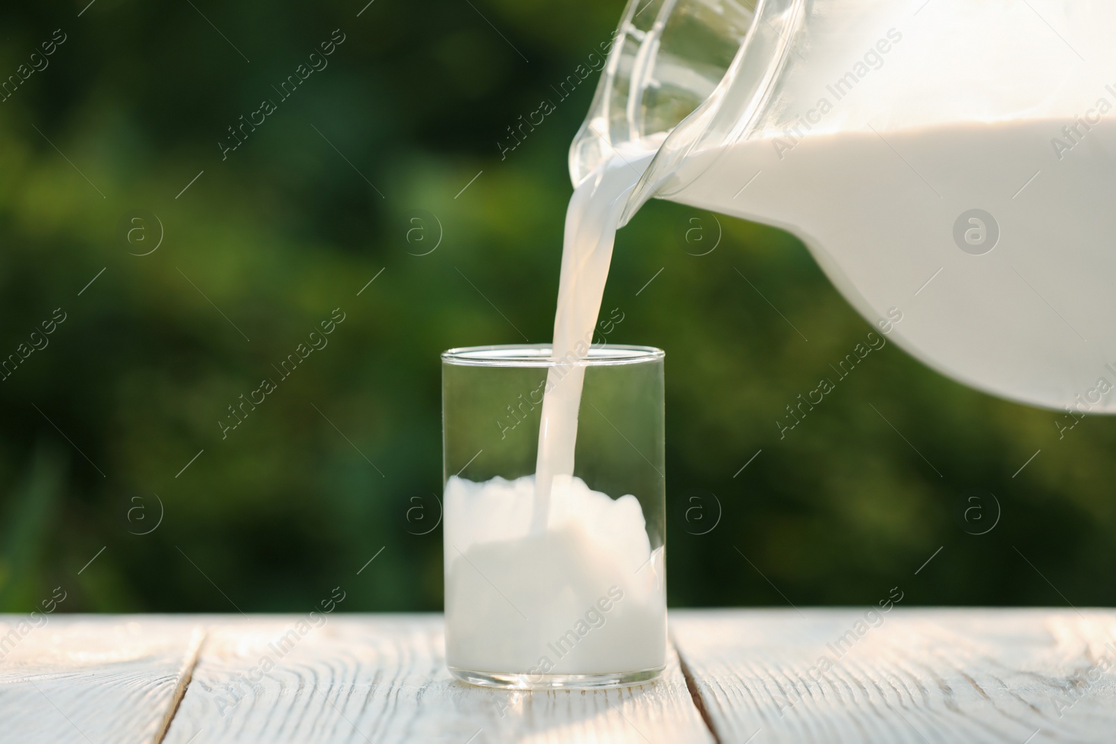 Photo of Pouring tasty fresh milk from jug into glass on white wooden table, closeup