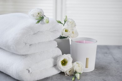 Photo of Scented candle, folded towels and eustoma flowers on gray marble table