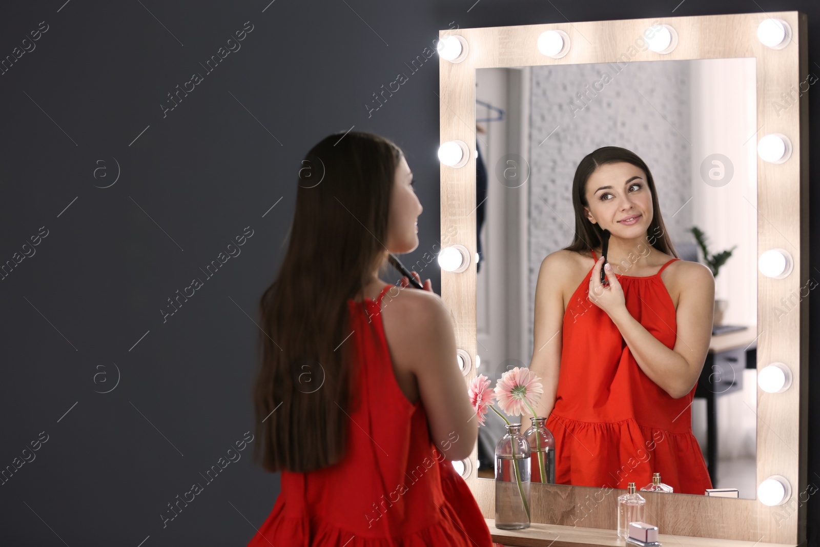 Photo of Young beautiful woman applying makeup near mirror