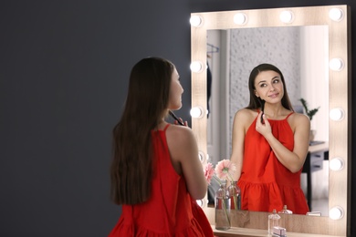 Photo of Young beautiful woman applying makeup near mirror