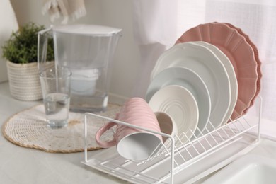 Drainer with different clean dishware and cup on light table indoors