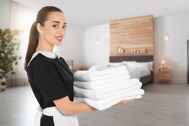 Image of Beautiful chambermaid with clean folded towels in hotel room