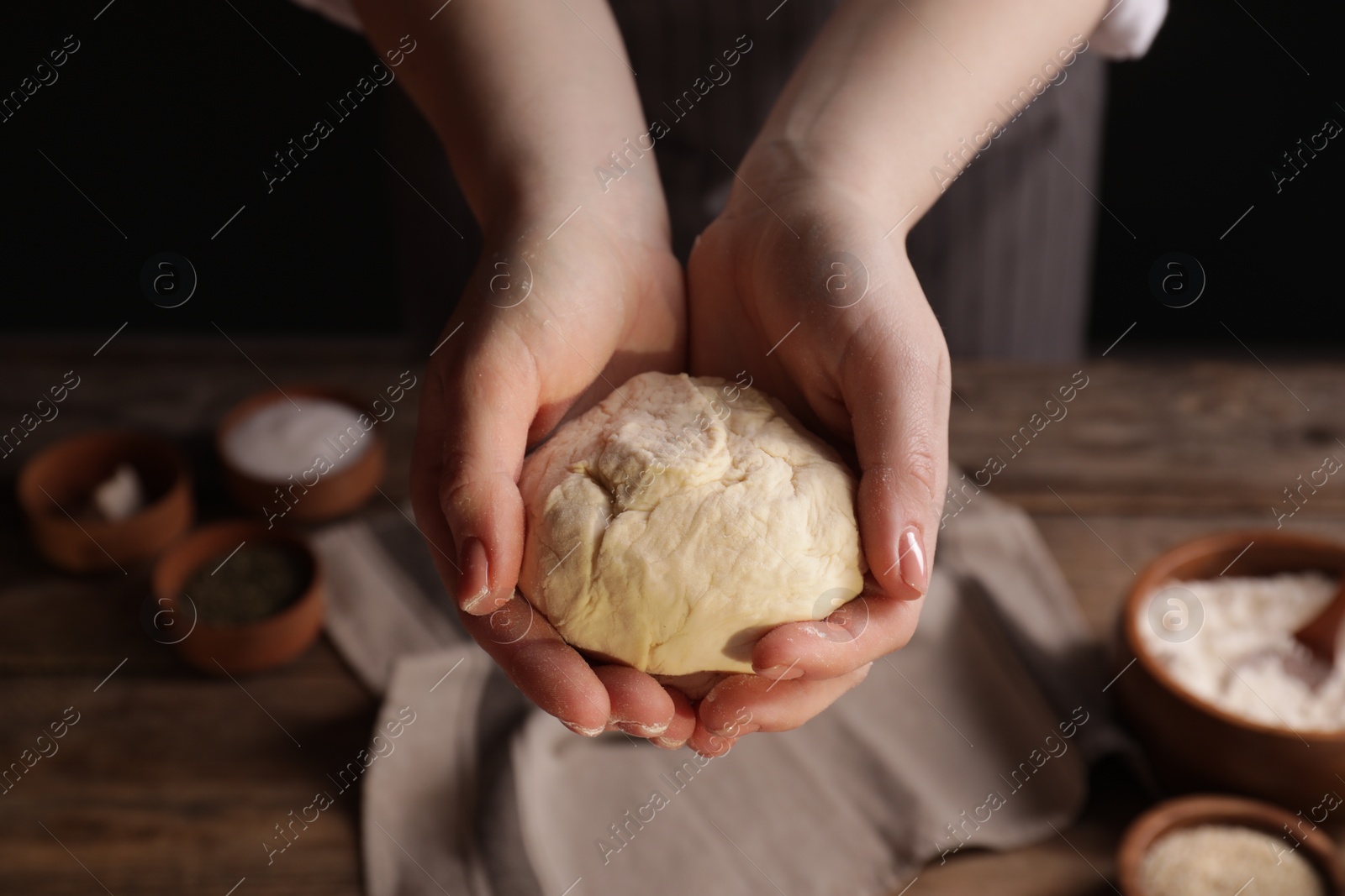Photo of Woman with fresh dough at wooden table with ingredients, closeup. Cooking traditional grissini