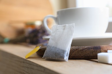 Photo of Tea bag and cup on wooden table indoors, closeup