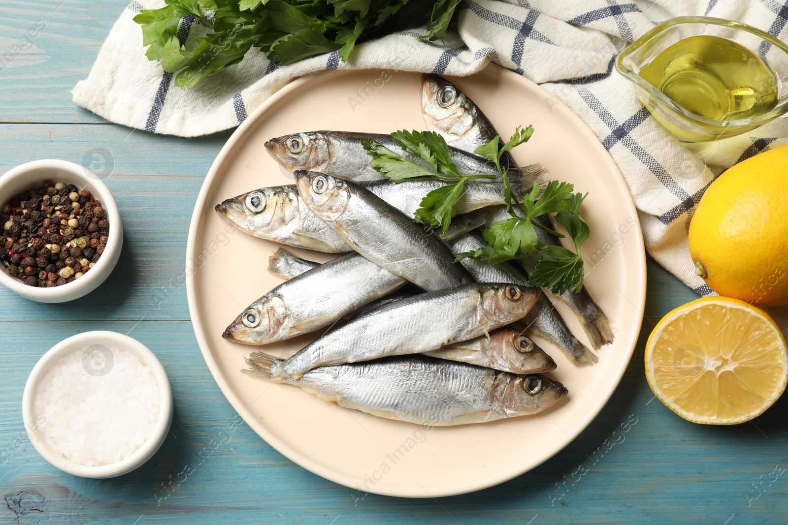 Photo of Fresh raw sprats, parsley and other products on light blue wooden table, flat lay