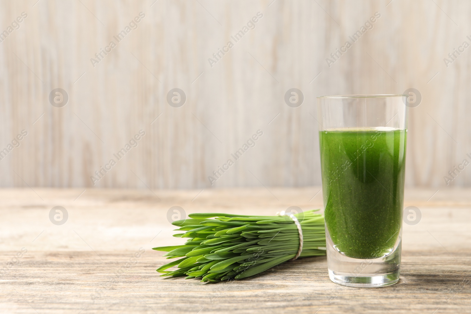 Photo of Wheat grass drink in shot glass and fresh green sprouts on wooden table, closeup. Space for text