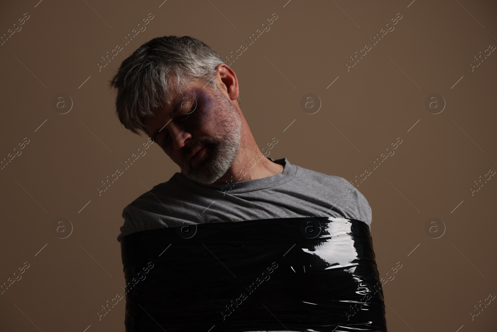 Photo of Beaten man tied with duct tape on beige background. Hostage taking