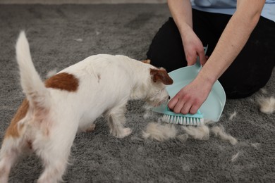 Photo of Man with brush and pan removing pet hair from carpet, closeup
