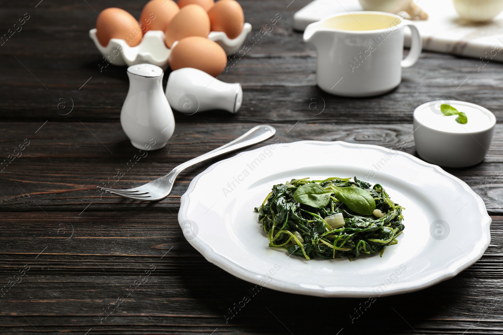 Photo of Plate with tasty cooked spinach on black wooden table. Healthy food