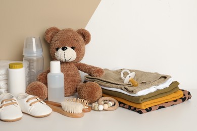 Baby clothes, toy bear and accessories on white table