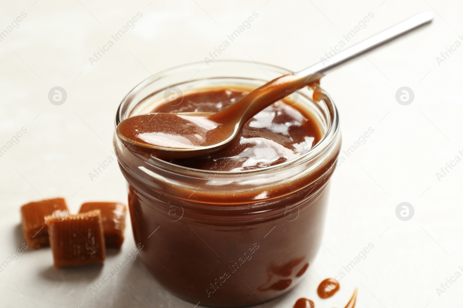 Photo of Jar with tasty caramel sauce and spoon on light background