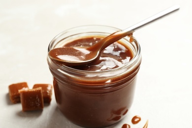 Photo of Jar with tasty caramel sauce and spoon on light background