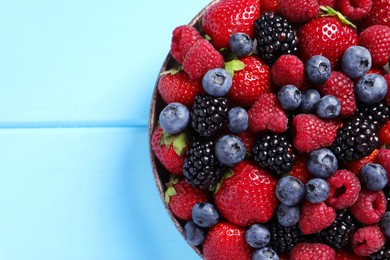 Different fresh ripe berries in bowl on light blue wooden table, top view. Space for text