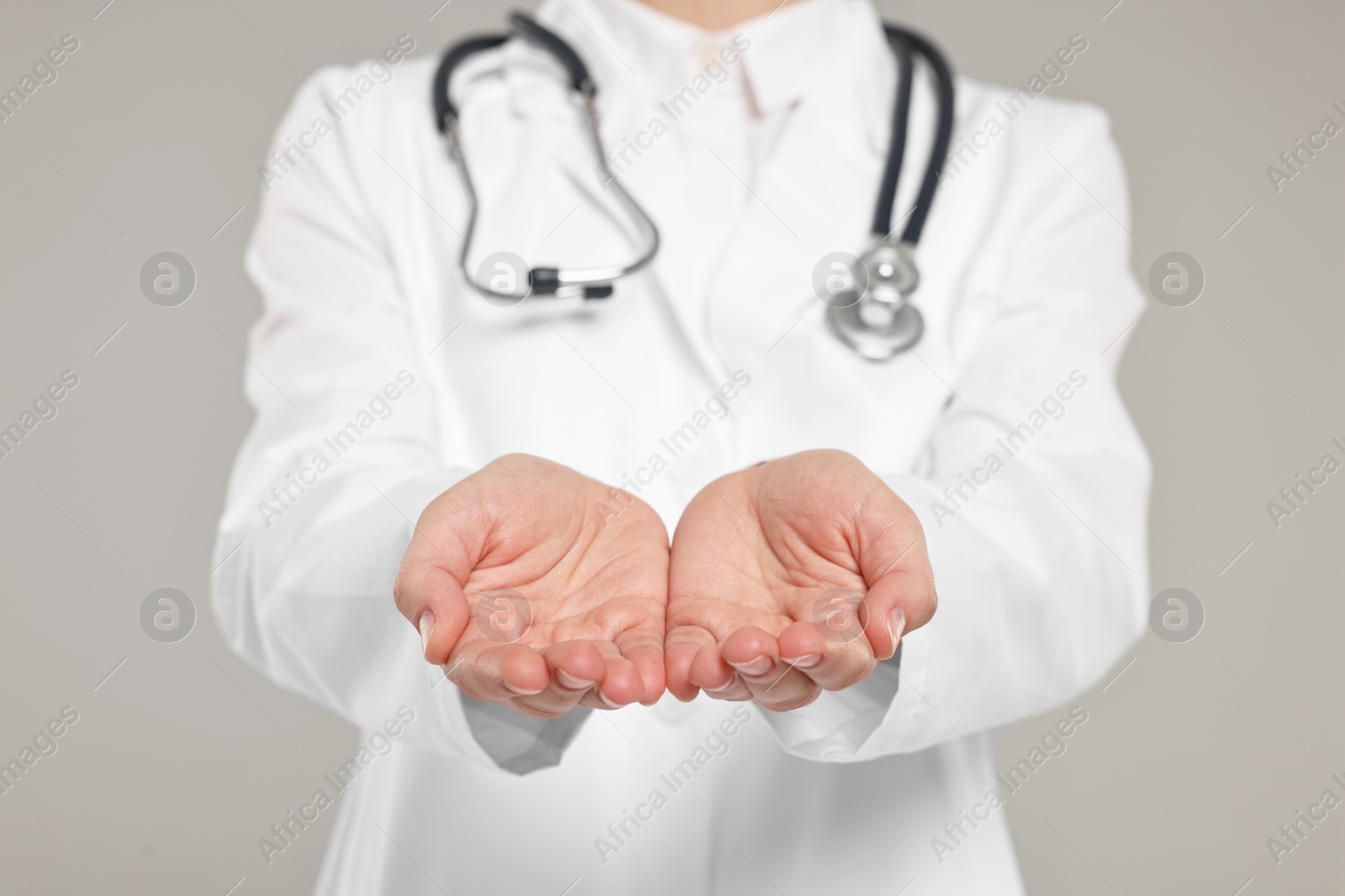 Photo of Doctor with stethoscope holding something on grey background, closeup