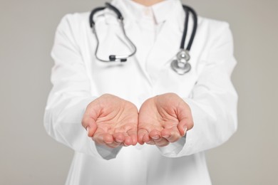 Doctor with stethoscope holding something on grey background, closeup