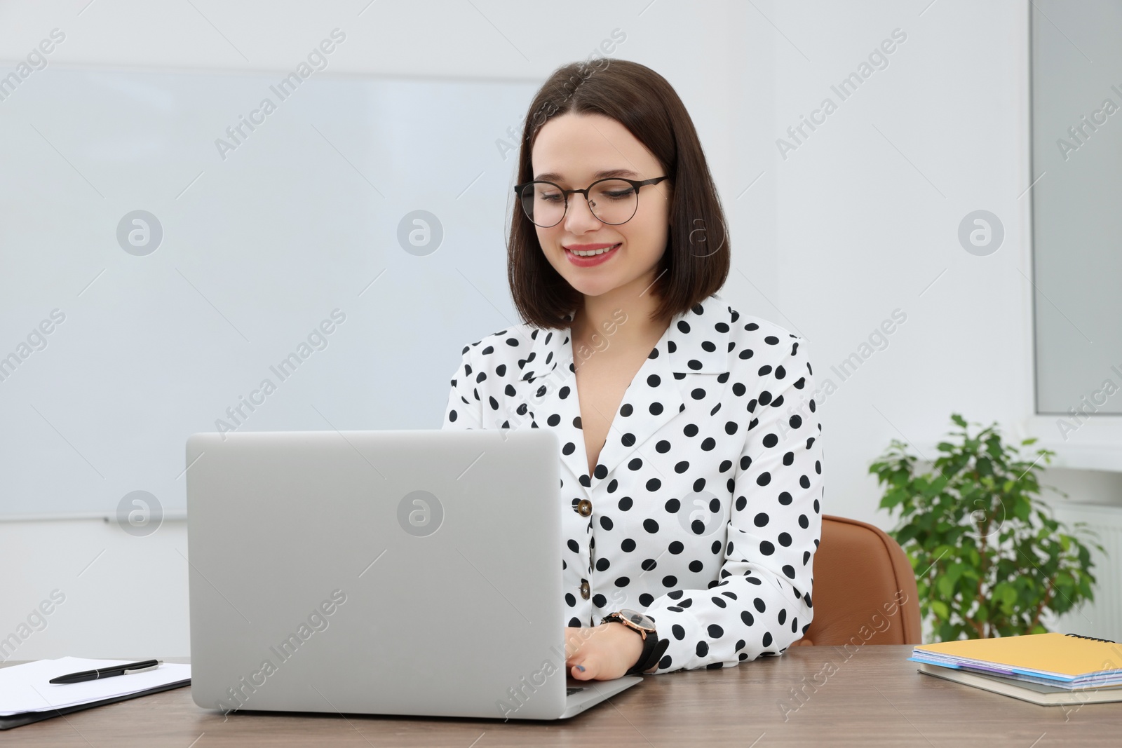 Photo of Happy young intern working with laptop at table in modern office