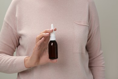 Photo of Woman holding nasal spray against light grey background, closeup