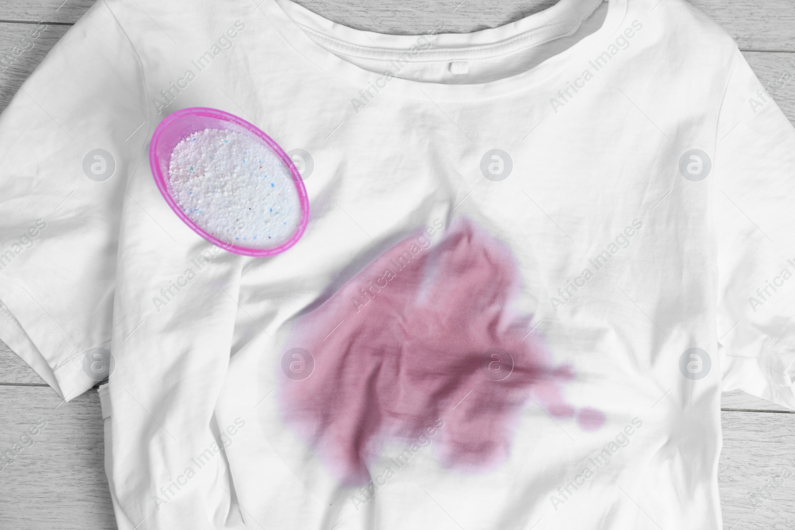 Photo of White t-shirt with stain and powdered detergent on wooden surface, top view. Hand washing laundry