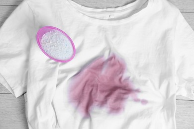 Photo of White t-shirt with stain and powdered detergent on wooden surface, top view. Hand washing laundry