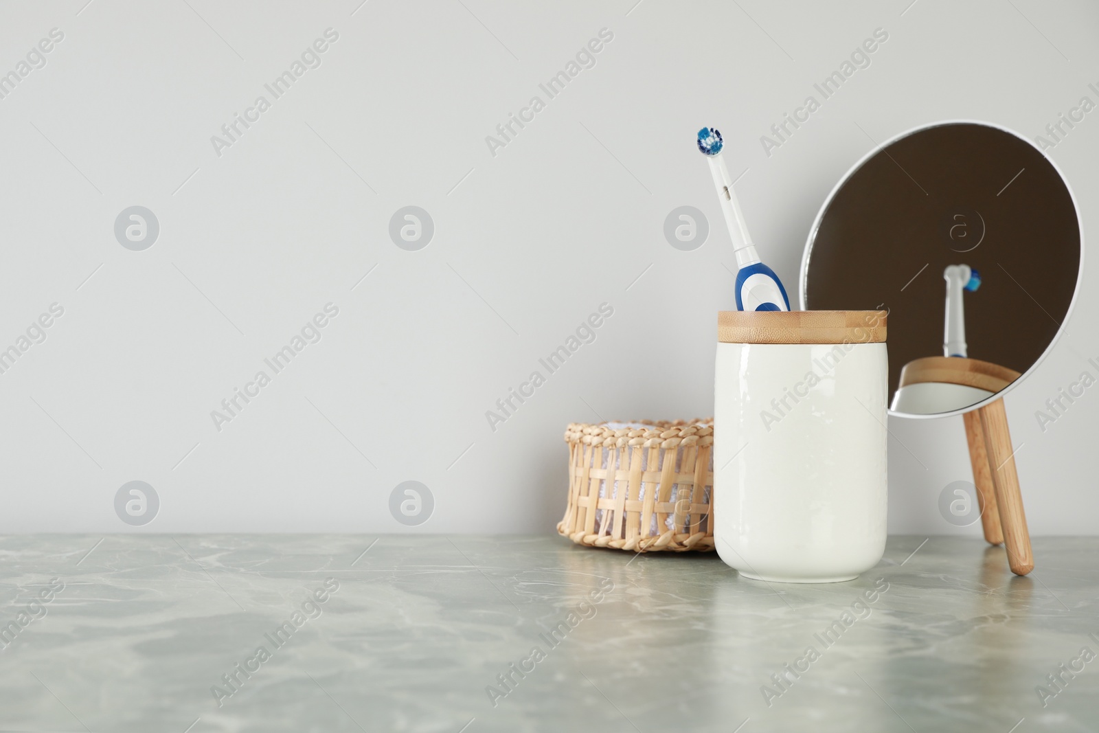 Photo of Electric toothbrush in holder, mirror and towel on light grey marble table near white wall. Space for text