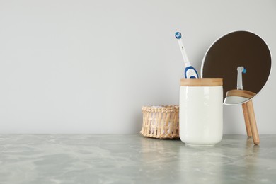 Electric toothbrush in holder, mirror and towel on light grey marble table near white wall. Space for text