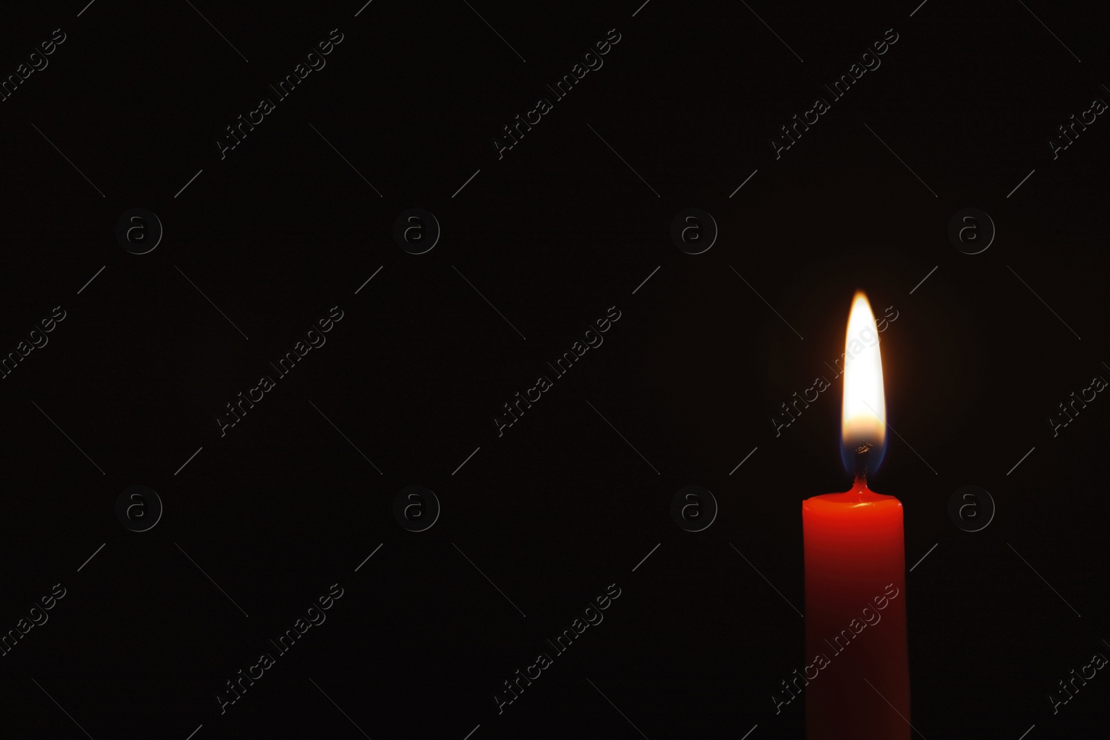 Photo of Wax candle burning on black background, closeup