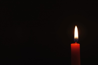 Photo of Wax candle burning on black background, closeup