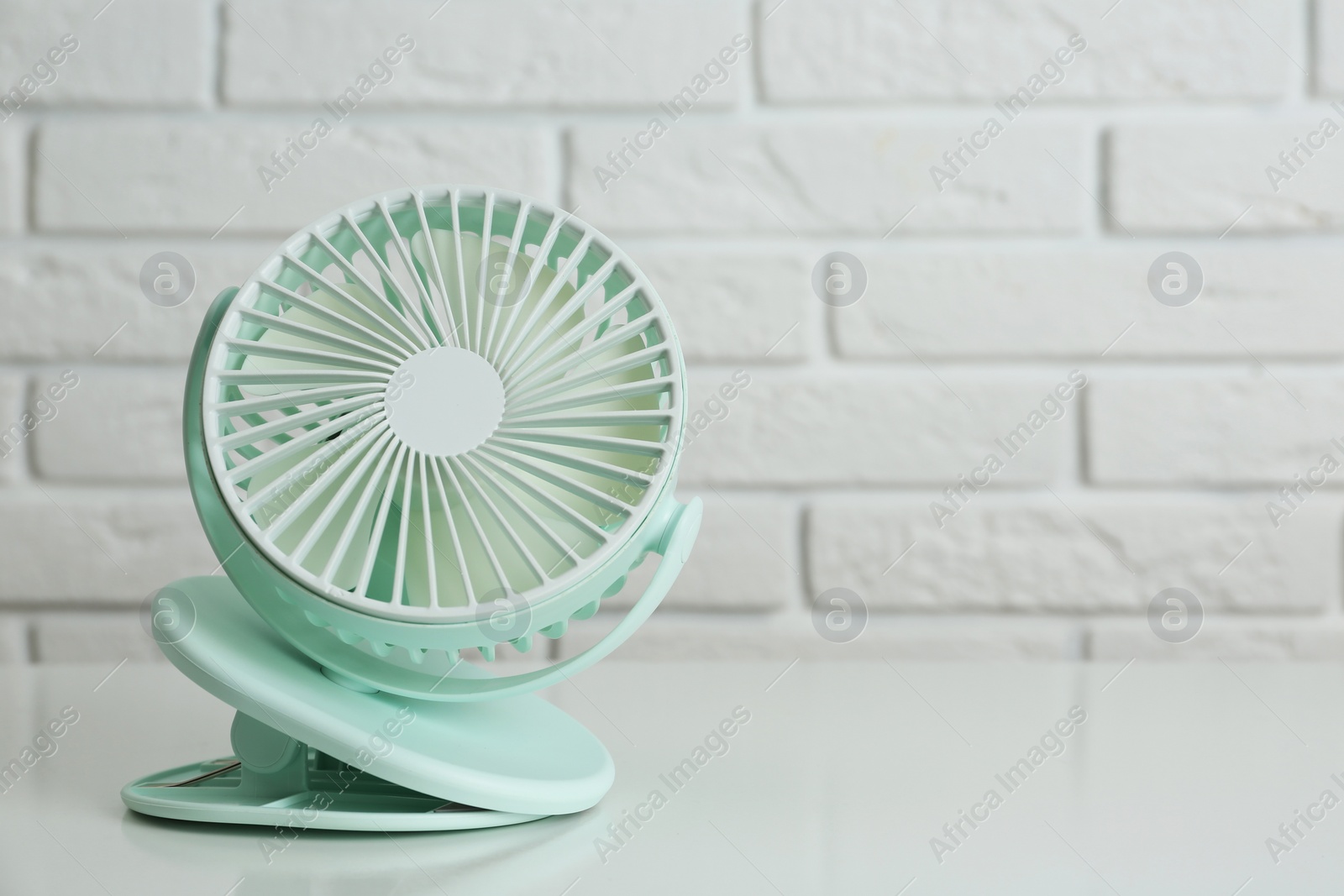 Photo of Portable fan on table near white brick wall, space for text. Summer heat