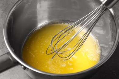 Photo of Whisk above saucepan with melting butter on table, closeup