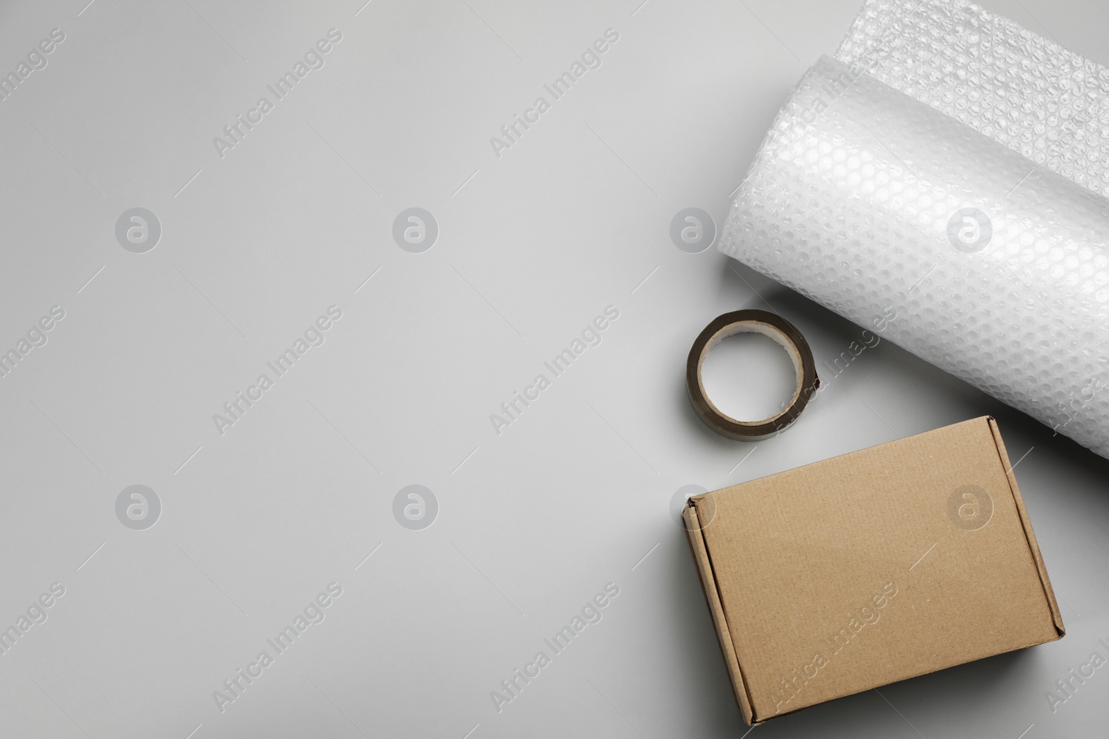 Photo of Bubble wrap roll, cardboard box and tape on light background, flat lay. Space for text