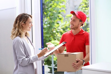 Photo of Young woman signing documents after receiving parcel from courier on doorstep