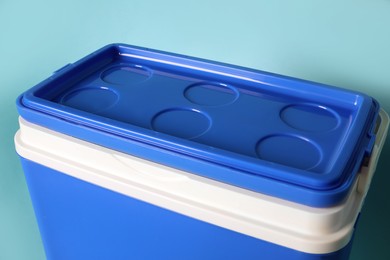 Photo of Closed blue plastic cool box on turquoise background, closeup