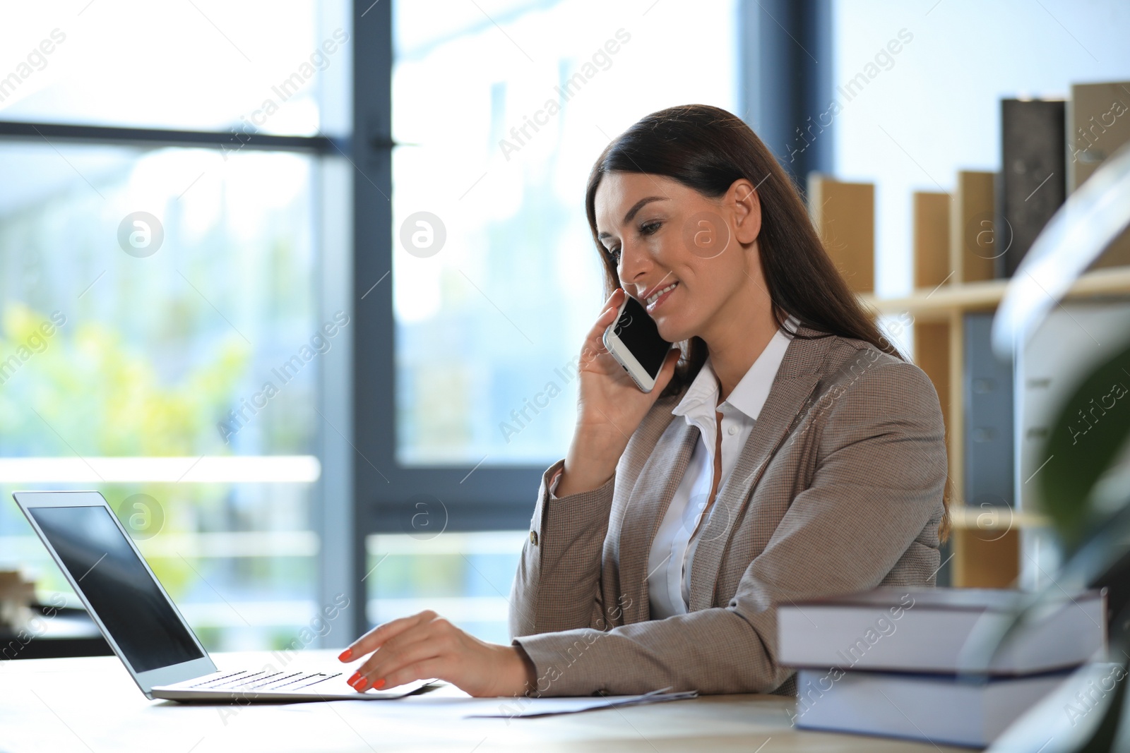 Photo of Female business trainer talking on phone while working with laptop in office