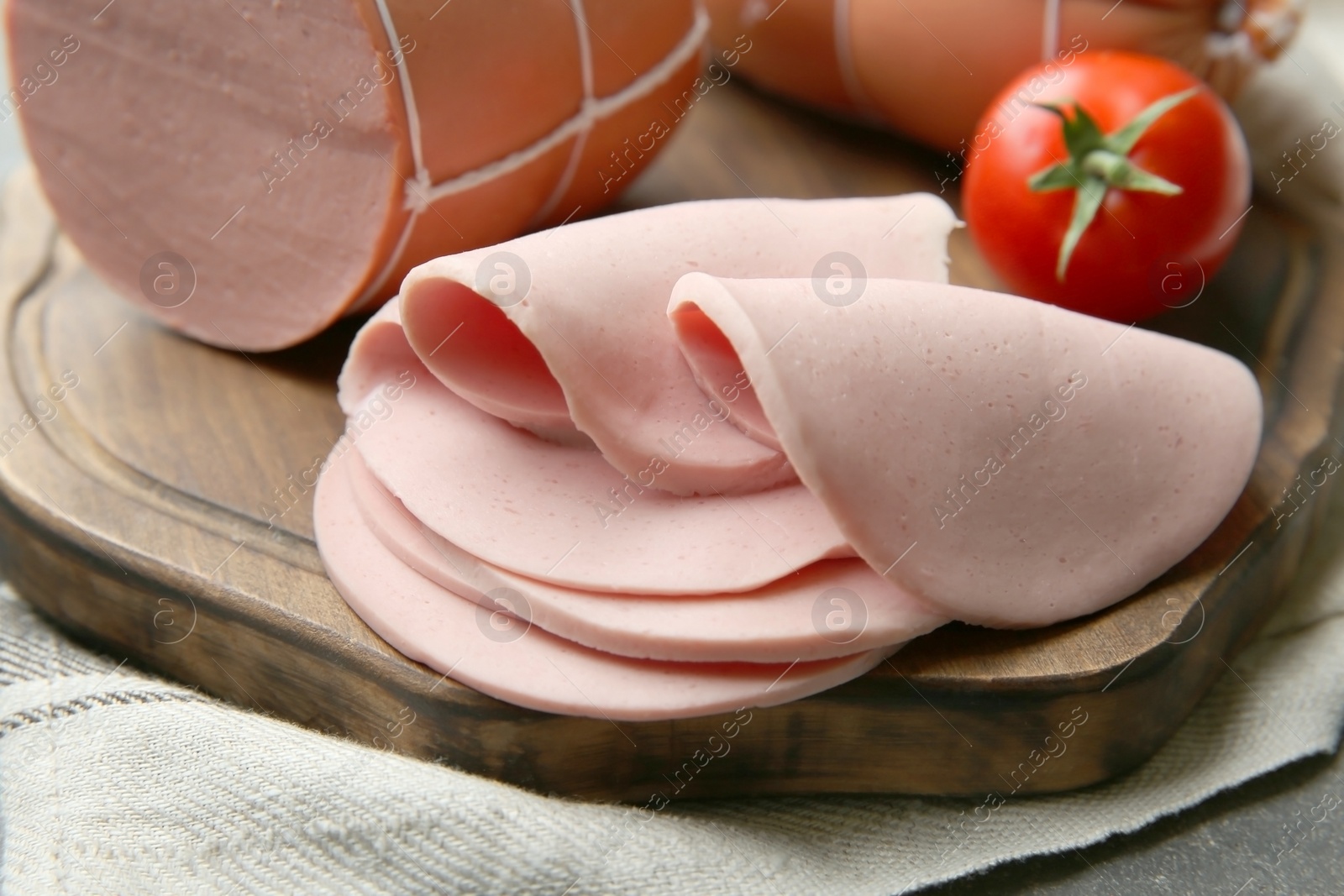 Photo of Board with tasty boiled sausages and tomato on grey table, closeup