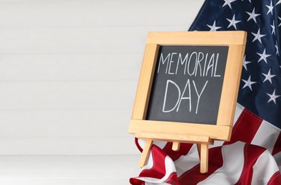 Photo of Blackboard with phrase Memorial Day and American flag on white wooden table, space for text