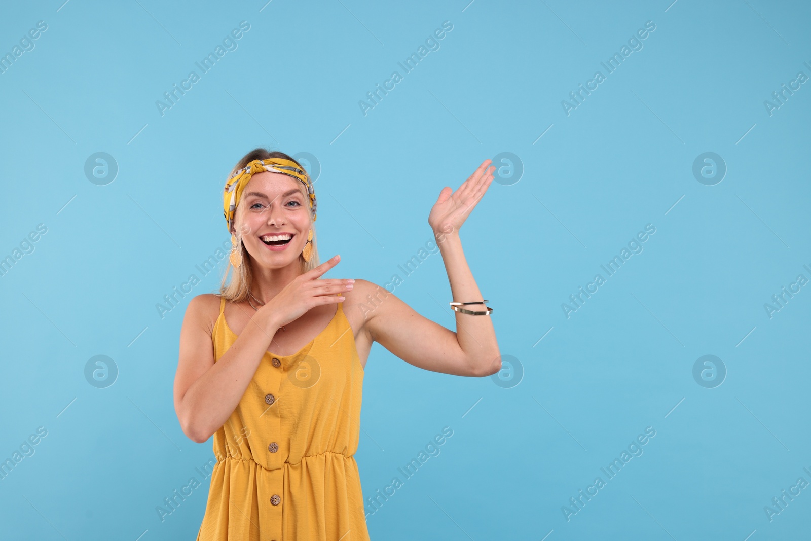 Photo of Portrait of happy hippie woman showing at something on light blue background. Space for text