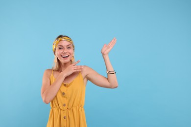 Photo of Portrait of happy hippie woman showing at something on light blue background. Space for text